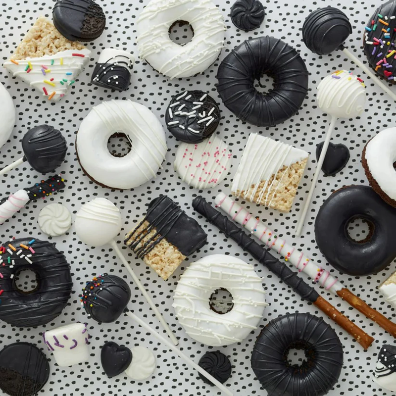 Assorted Black and White themed treats including donuts, cakes, and cookies on a polka dot background.