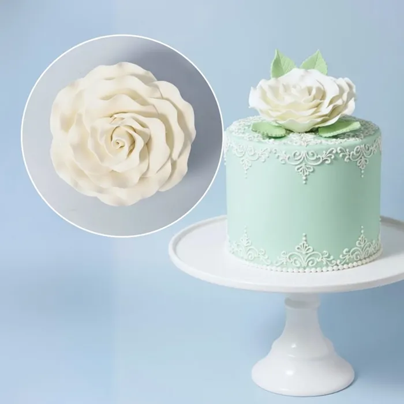 Mint green cake with white rose decoration on a white stand against a light blue background