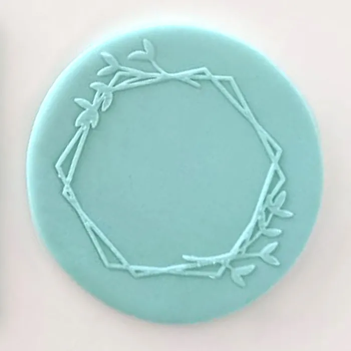 A geometric wreath with leafy branches design shown on a teal fondant icing plaque