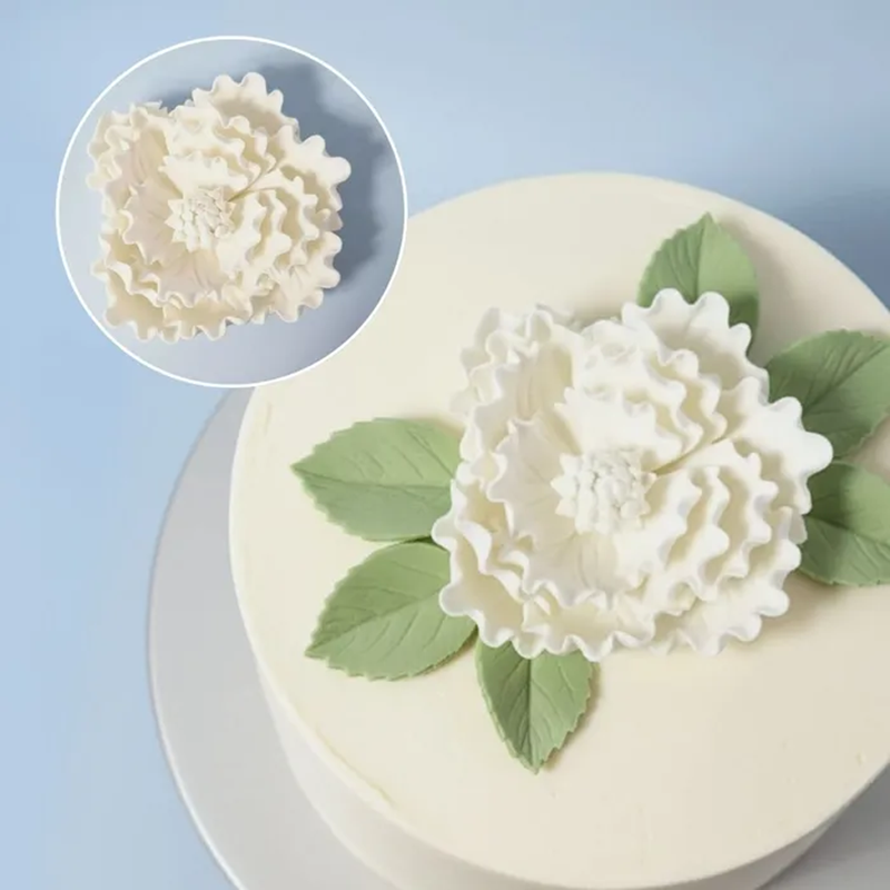 Decorative white icing Peony flower on a cake with a close-up inset of the flower.