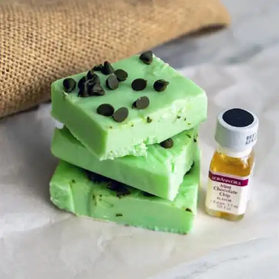 A dram bottle of Lorann Oils Mint Chocolate Chip Flavouring alongside green coloured fudge decorated with brown chocolate chips.