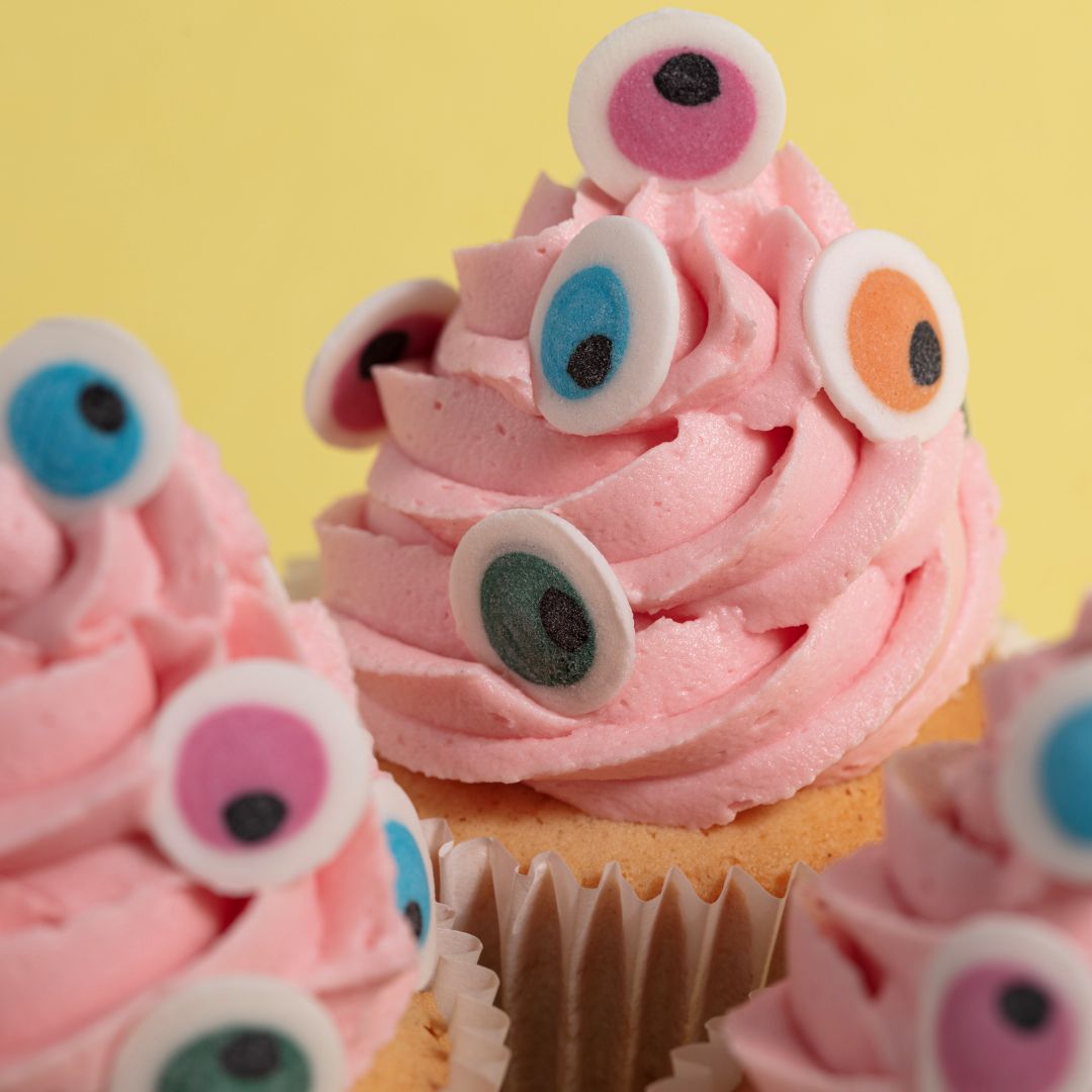 Cupcakes with pink frosting and colorful candy eyes on a yellow background