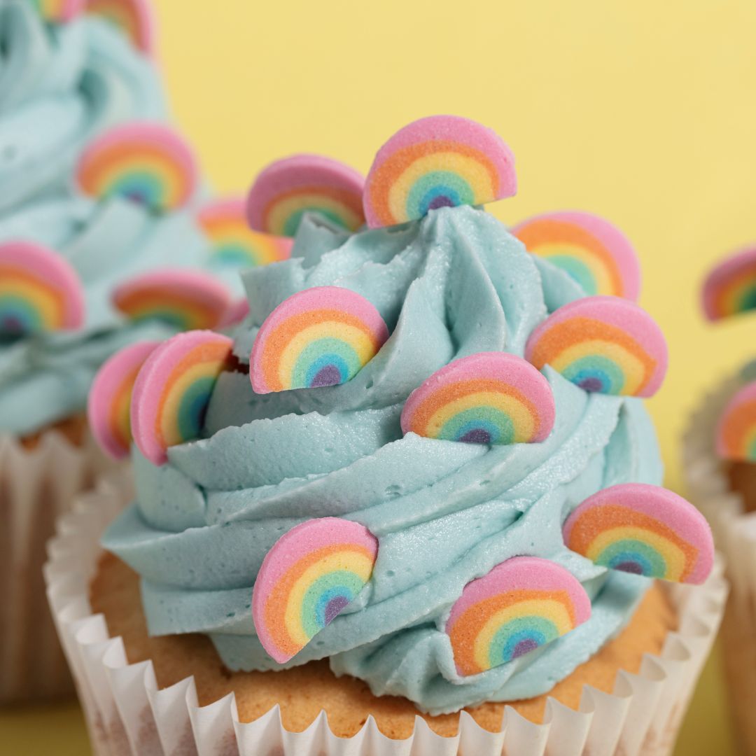 Cupcake with blue frosting and rainbow decorations on a yellow background