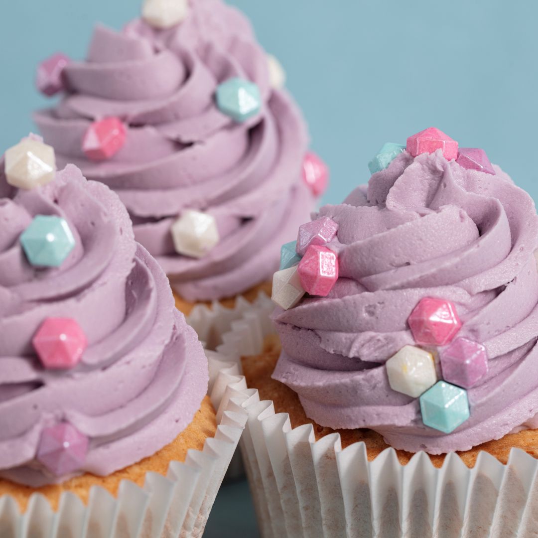 Cupcakes with purple frosting and colorful diamond sprinkles on a light blue background