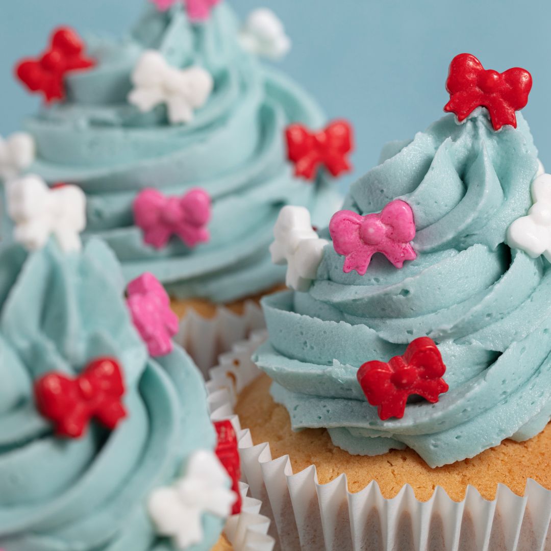 Cupcakes with blue frosting, red and pink bow decorations on a light blue background