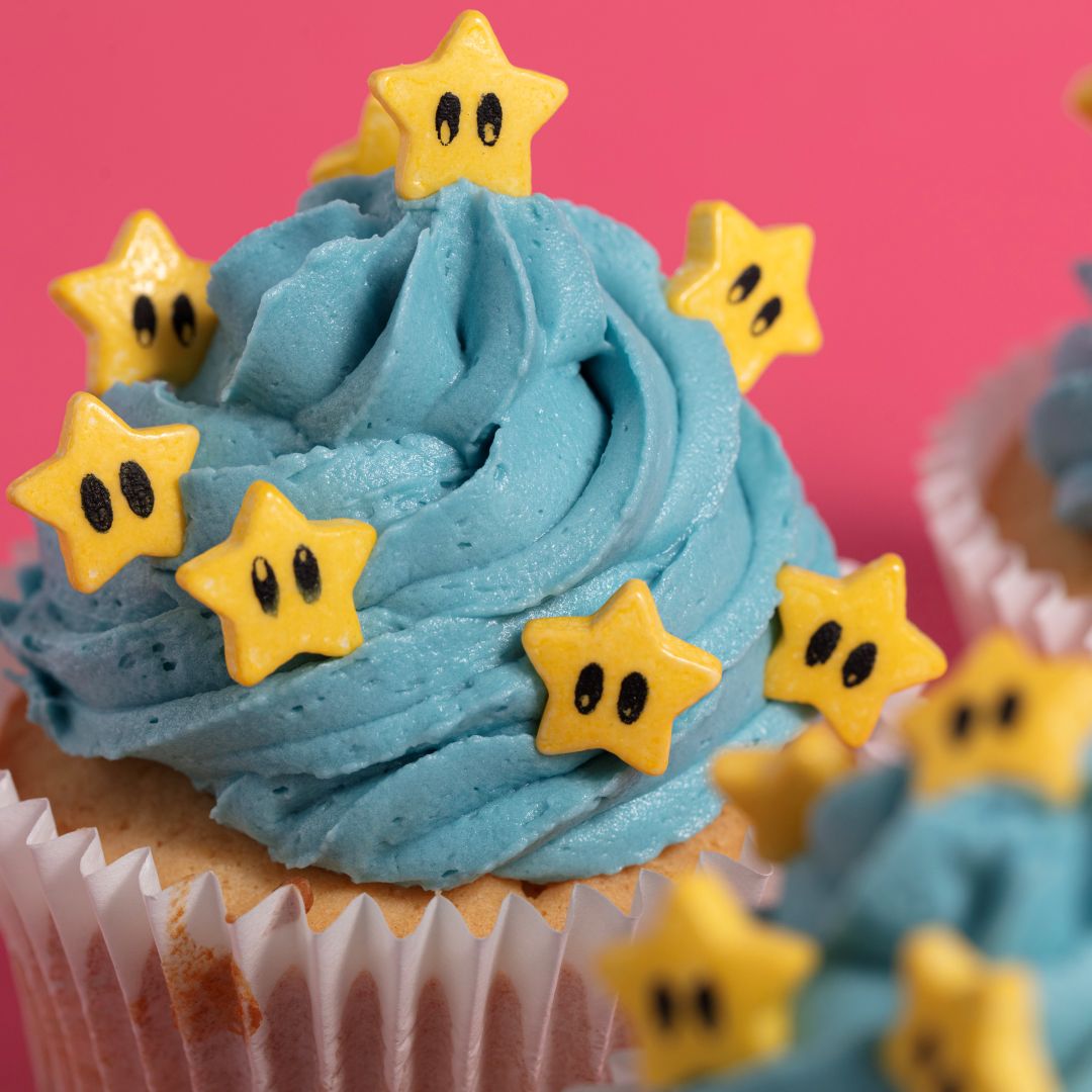 Cupcake with blue frosting and yellow star-shaped decorations on a pink background