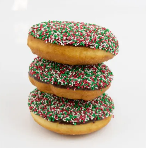 Three stacked donuts with golden-brown fried dough, chocolate glaze, and red, green, and white sprinkles on a white background.