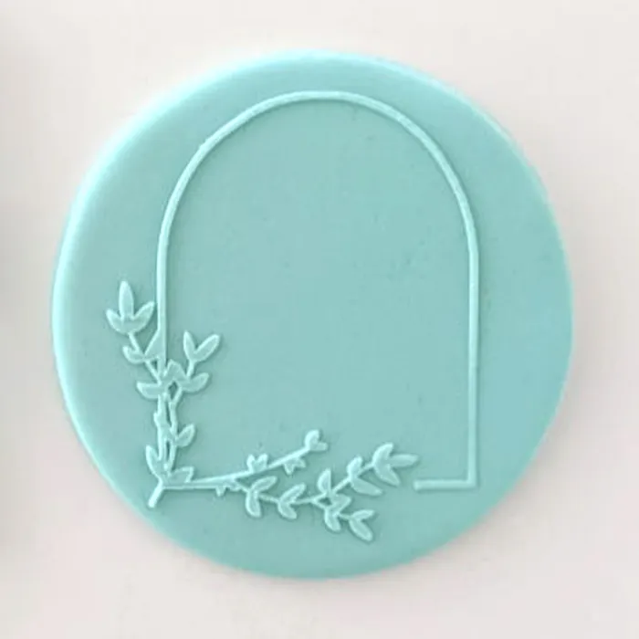 A round, light aqua blue fondant icing circle featuring a debossed arch and leafy vine design in the lower left, shown on a plain off-white background.