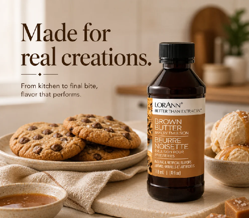 A bottle of LorAnn Better Than Extracts Brown Butter flavor food flavouring emulsion stands on a countertop beside chocolate chip cookies, a small bowl of caramel sauce, and pastries in a warm kitchen setting. Large text on the left reads, 'Made for real creations.