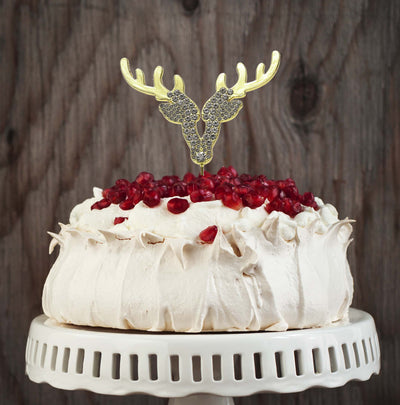 Decorative cake with pomegranate seeds and a gold deer antler topper on a wooden background