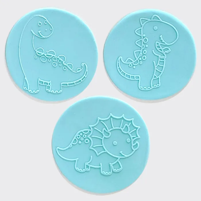 Three circular light blue fondant circles featuring embossed dinosaur designs, arranged on a plain light gray background.