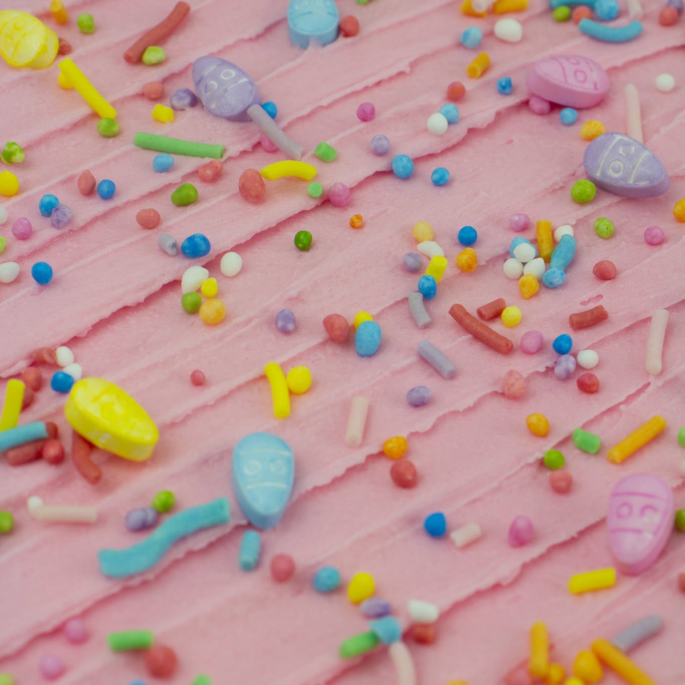 Close-up of pink frosted cake or pastry topped with colorful candy sprinkles and pastel candy pieces.