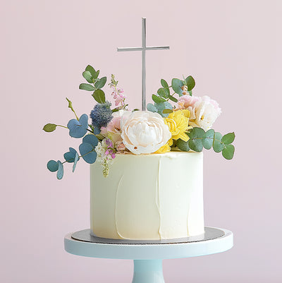 Silver metal cross topper standing tall above floral bouquet cake