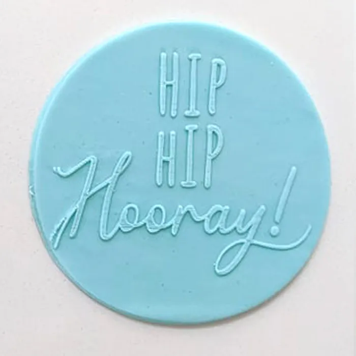 A round light blue fondant icing plaque with the words 'HIP HIP Hooray!' embossed in white, shown on a plain off-white background.