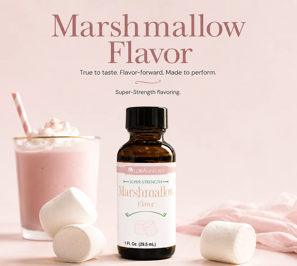An amber glass bottle of Lorann Marshmallow Flavor Super Strength flavoring, styled on a soft pink background with a pink drink, whipped cream, and marshmallows.