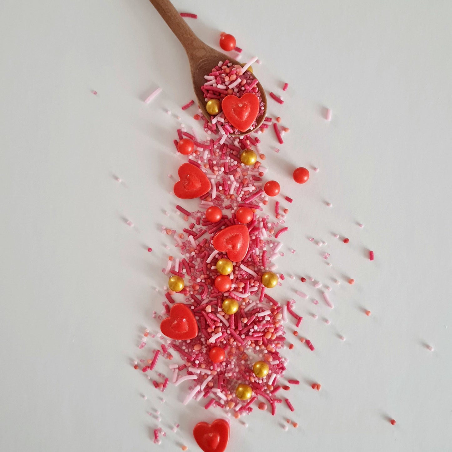 Wooden spoon with red heart-shaped candies and pink sprinkles on a white background
