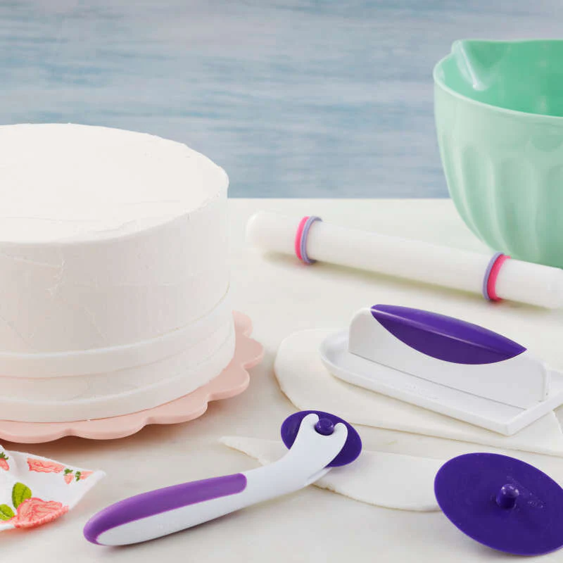 Example of an assortment of Wilton cake decorating tools including a cake turntable, rolling pin, and purple-handled tools.