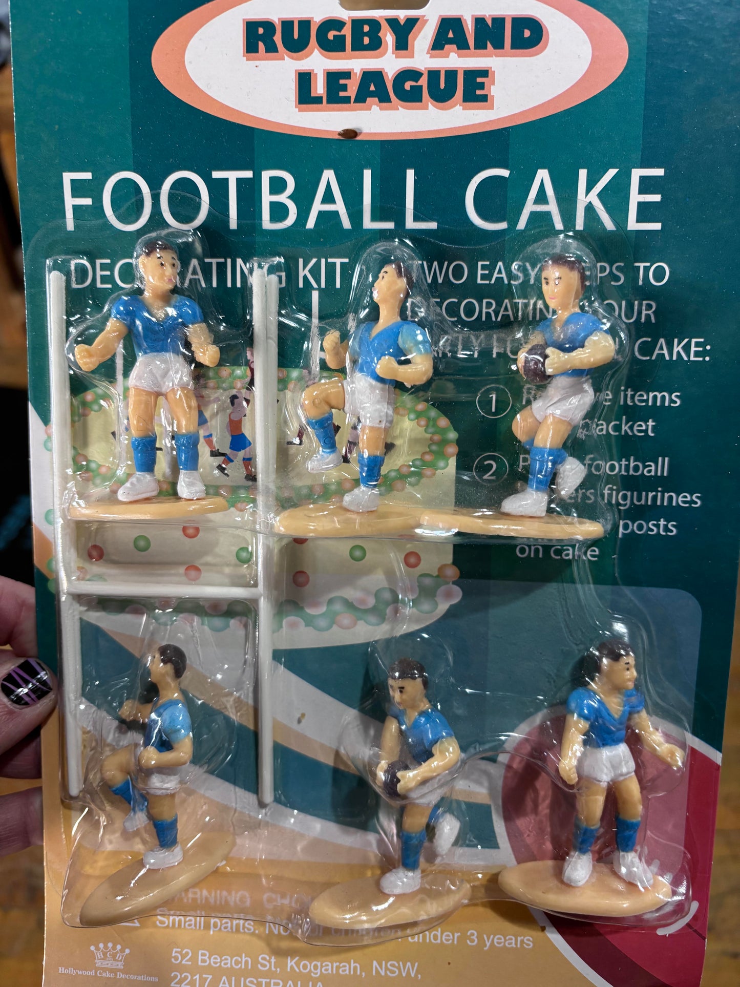 Rugby and League Football Cake decorating kit in its original retail packaging, featuring six small rugby player figurines dressed in blue and white jerseys, packaged on a green and white cardboard backing.