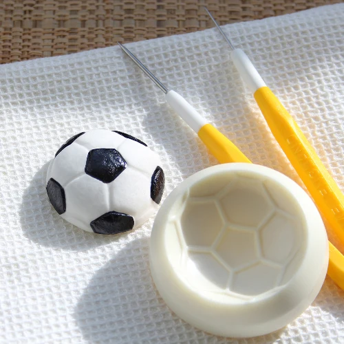 Soccer ball-shaped mold and tools on a textured surface with icing example of a soccer ball