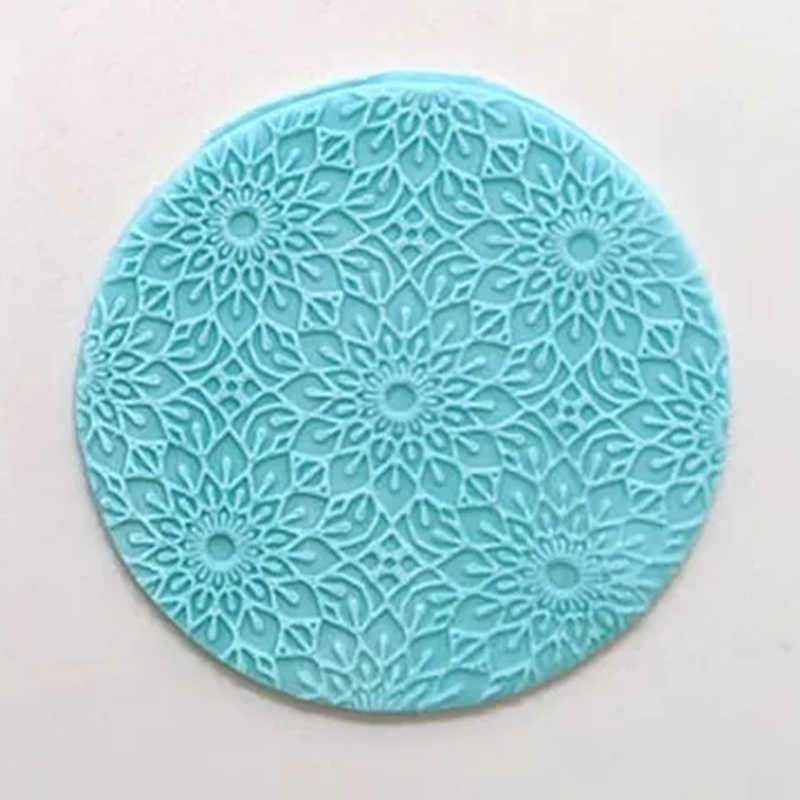 A round turquoise blue fondant plaque with an intricate floral mandala embossed pattern, shown on a plain off-white background.
