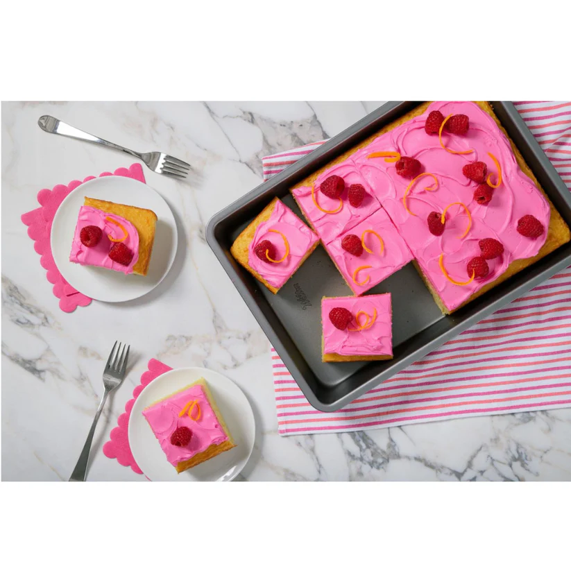 Pink frosted cake in Wilton baking pan with raspberries on a marble surface