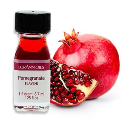 A small bottle labeled 'Pomegranate Flavor' by Lorann Oils, next to a pomegranate and some of its seeds scattered around.