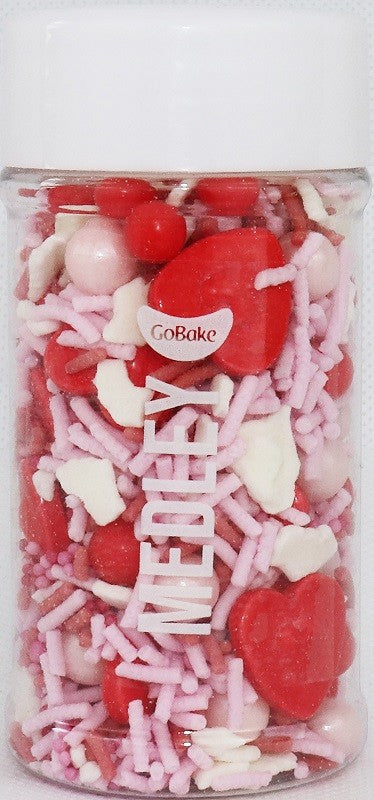 A clear jar filled with pink and red sprinkles, some shaped like hearts, with a white lid on top