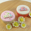 Two decorated cupcakes on a wooden surface, one with pink frosting and white fondant lettering that reads BABY, and the other with white frosting and pink fondant lettering that reads BABY. Four white and yellow flower decorations are placed in front.