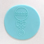 A light blue circularteal fondant disc featuring an embossed outline of a rattle with a bow, shown on a plain off-white background.