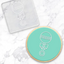 Circular cookie with a baby rattle design on a marble surface. Along with the debossing tool used to create it