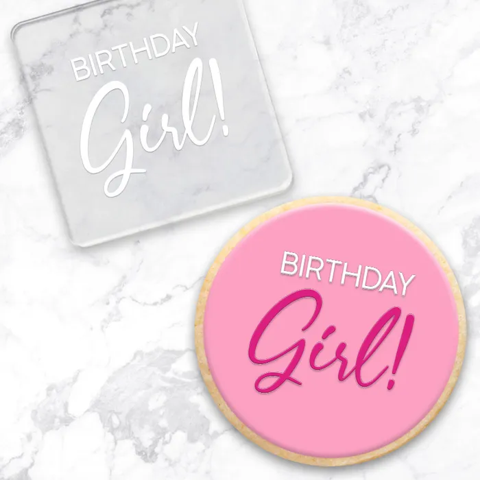Pink cookie with 'Birthday Girl!' text on a marble surface. With clear acrylic debosser tool used to make it