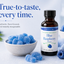A bottle of LorAnn Oils Blue Raspberry flavor stands next to a small bowl of blue raspberry candies on a light blue surface. Large text at the top reads, 'True-to-taste, every time.