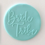 A round turquoise blue fondant plaque or sign with the words 'Bride Tribe' written in raised script, shown against a plain light background.