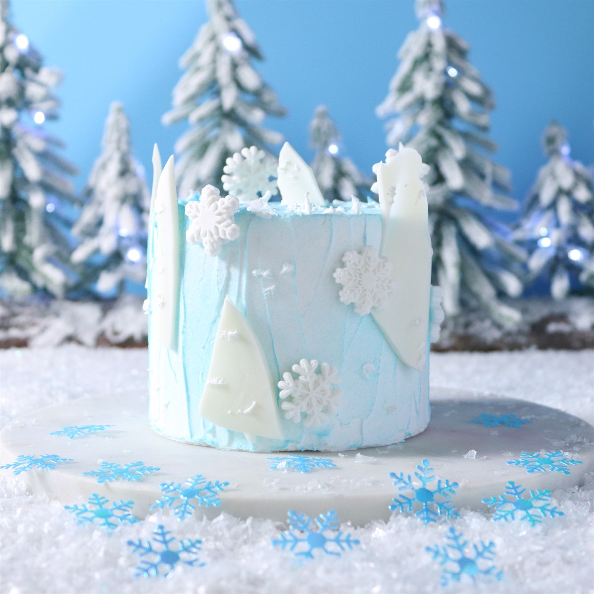 Decorative cake with winter theme featuring snowflakes and trees against a blue background