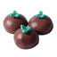 Three chocolate truffles with green holly decorations on a white background