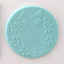 A round light blue fondant decorative plaque featuring an embossed floral wreath with a bow at the top, shown on a plain light background.