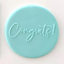 A round light blue fondant plaque featuring the word 'Congrats!' in cursive script, shown on a plain white background.