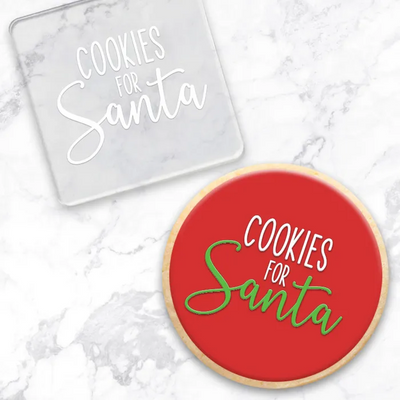 A clear acrylic debosser featuring the phrase 'COOKIES FOR Santa' in white lettering, shown on a white marble surface. Along with a finished cookie with a red center and the same phrase in white and green.