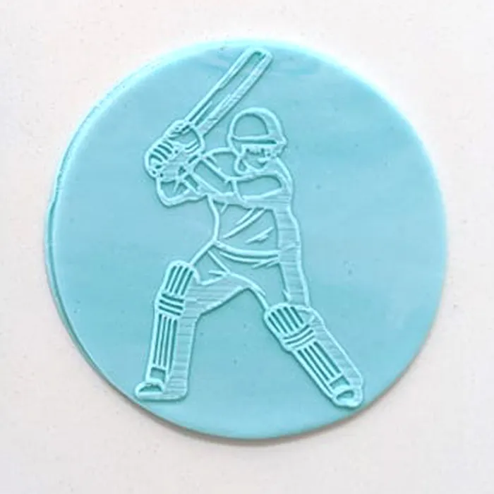 A circular light blue plaque of fondant icing featuring an embossed white outline of a cricket player holding a bat, shown on a plain off-white background.