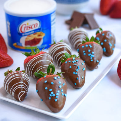 Chocolate-dipped strawberries with blue star sprinkles on a plate with Crisco container in the background.