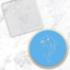 Dolphin design on a blue circle cookie with a clear acrylic debosser with the same design, on a marble background