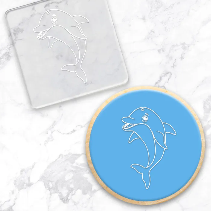 Dolphin design on a blue circle cookie with a clear acrylic debosser with the same design, on a marble background
