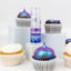 Cupcakes with colorful frosting and a bottle of Pixie Dust glitters on a white background