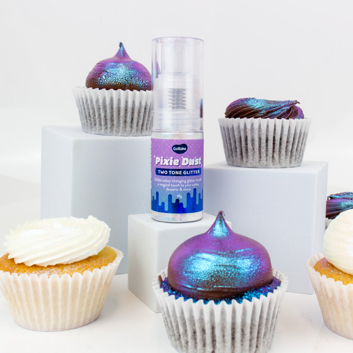 Cupcakes with colorful frosting and a bottle of Pixie Dust glitters on a white background