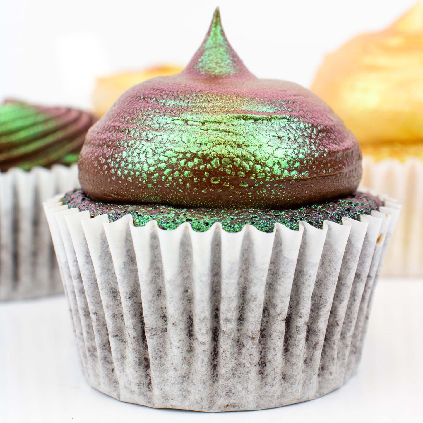 Cupcake with iridescent green and purple frosting on a white background