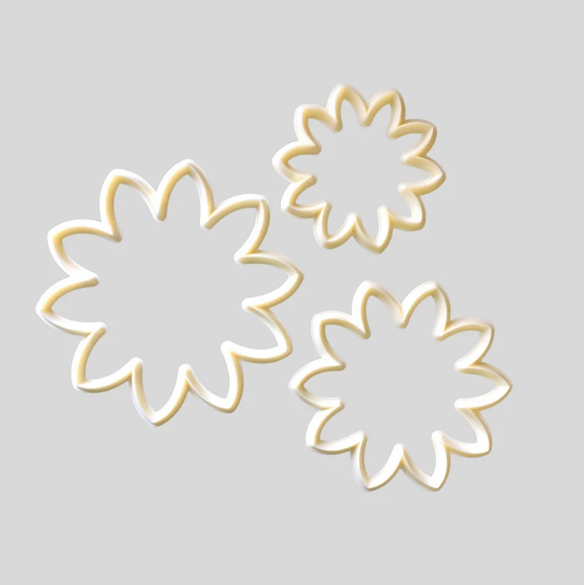 Three flower-shaped  cutters in different sizes, made of white ceramic with a glossy finish, arranged on a solid light gray background.