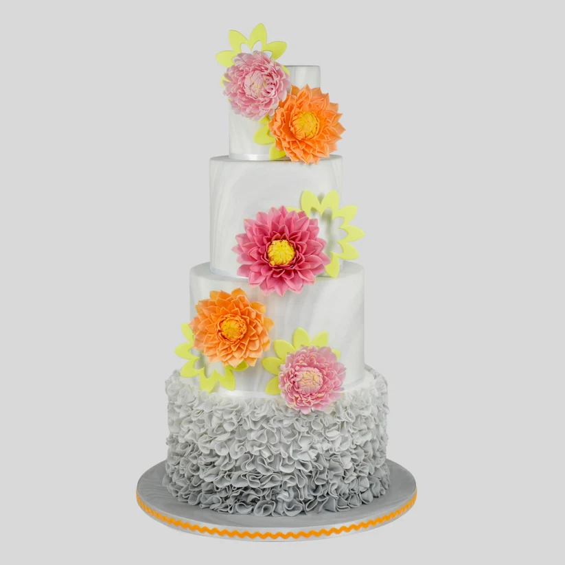 A three-tier white cake decorated with large pink, orange, and yellow sugar flowers, featuring a gray ruffled bottom border and a gray cake board, set against a solid gray background.
