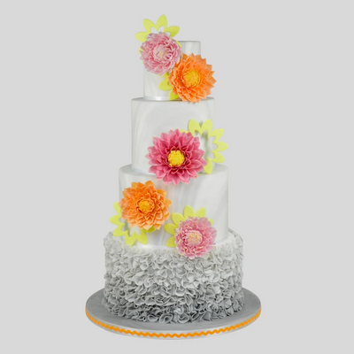 A three-tier white cake decorated with large pink, orange, and yellow sugar flowers, featuring a gray ruffled bottom border and a gray cake board, set against a solid gray background.