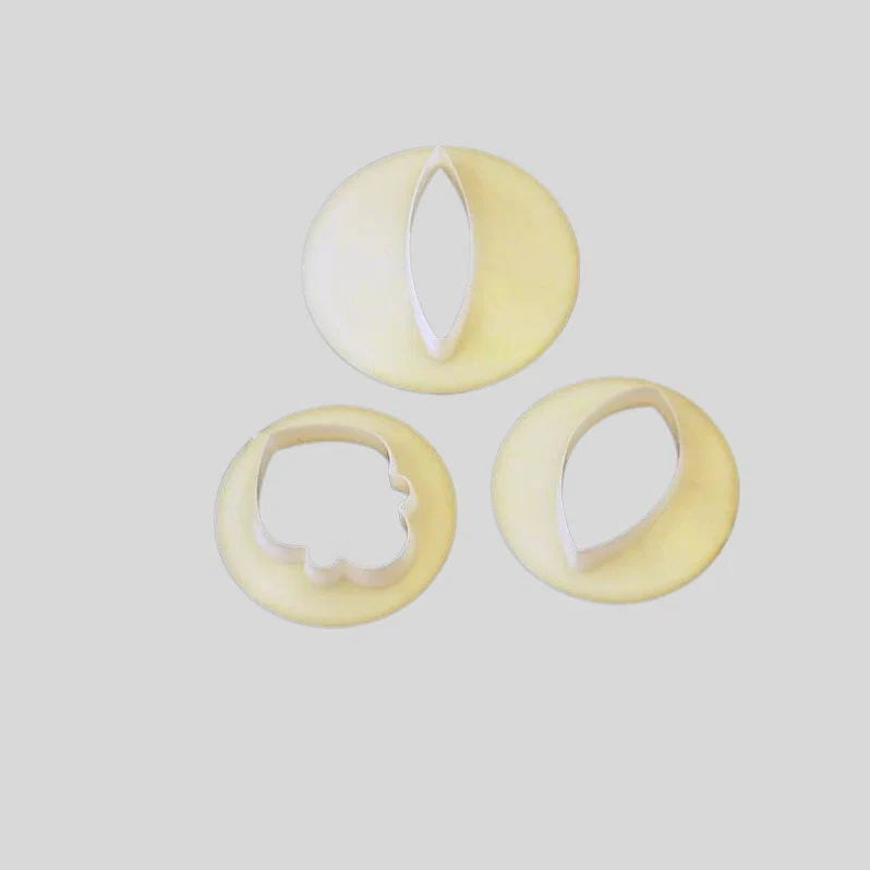 Three pale yellow plastic flower petal cutters in different shapes, arranged on a light gray background.
