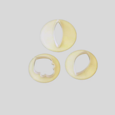 Three pale yellow plastic flower petal cutters in different shapes, arranged on a light gray background.